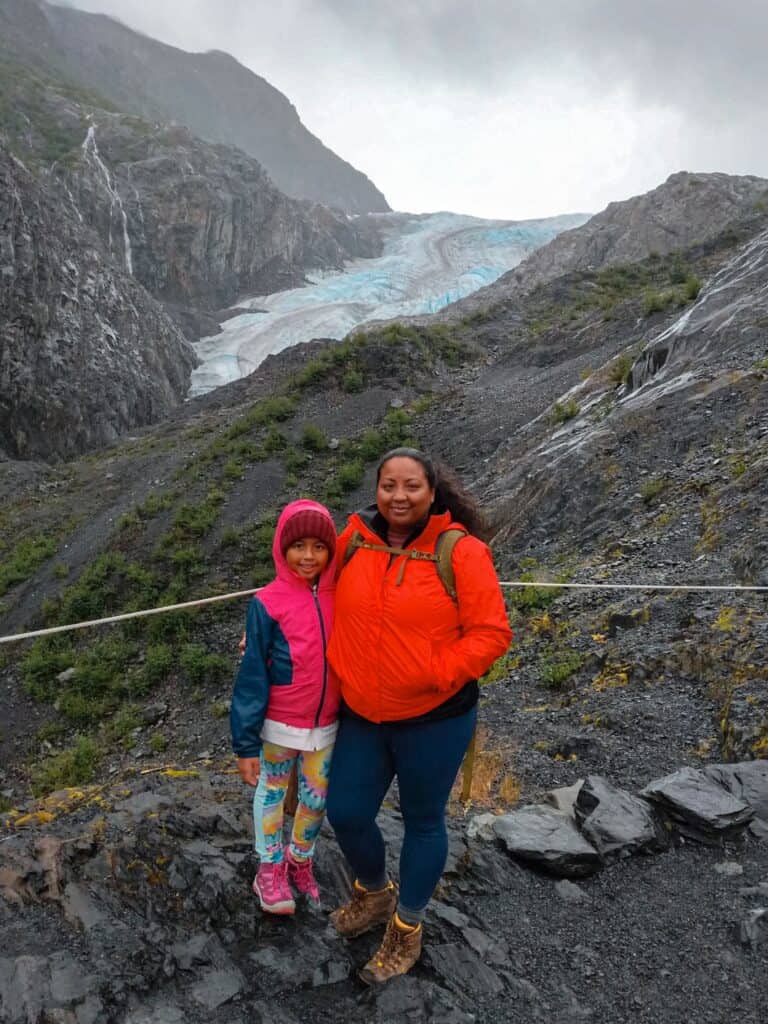 mother and daughter standing at an overlook with Kenai Fjords' Exit Glacier behind them 